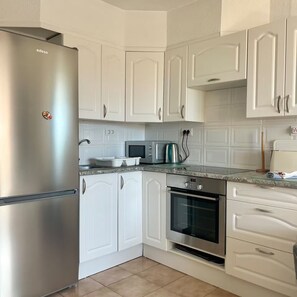A kitchen with white cabinets, a stainless steel refrigerator, a microwave, and an oven.