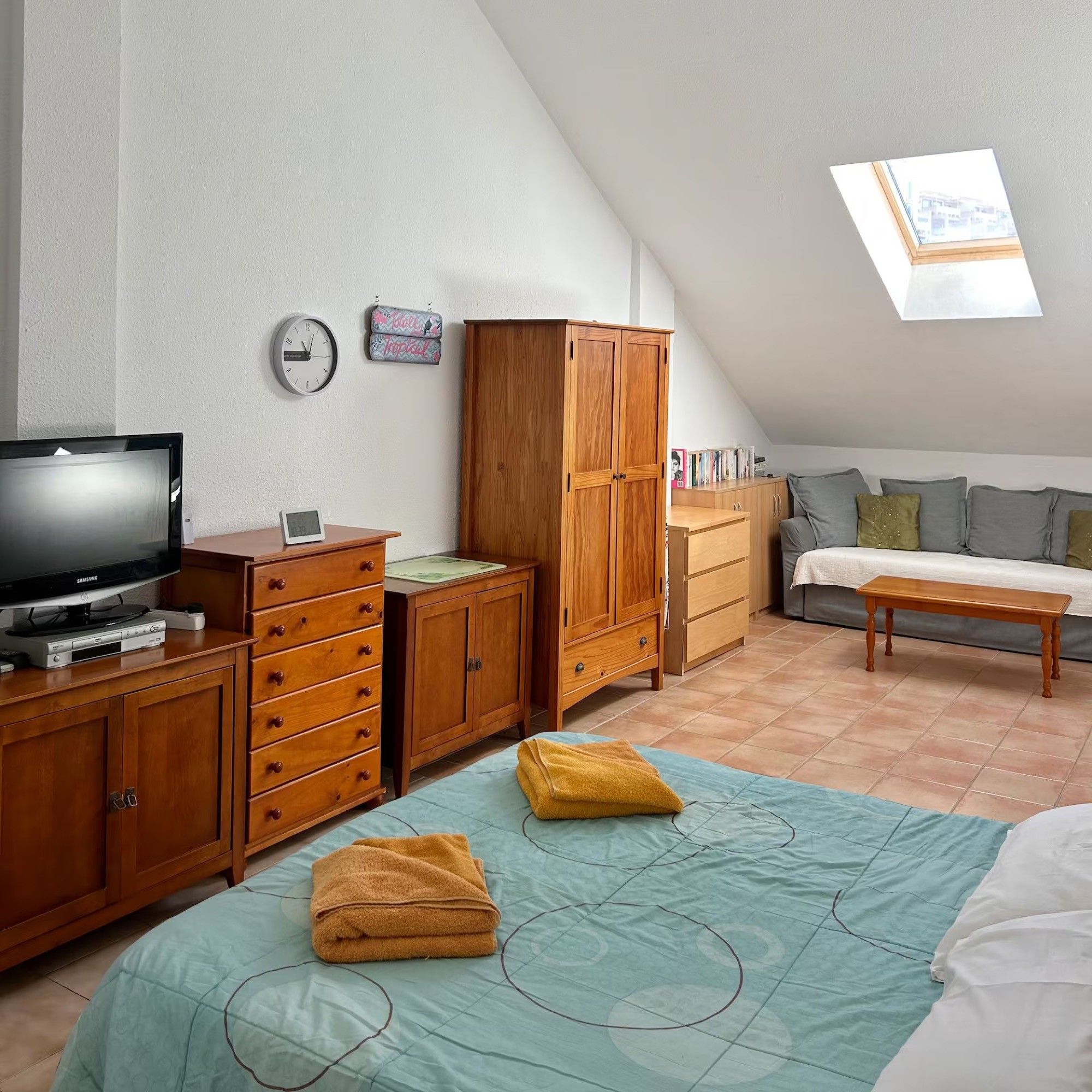 A bedroom with a bed, a TV, wooden furniture, a clock, and a skylight.
