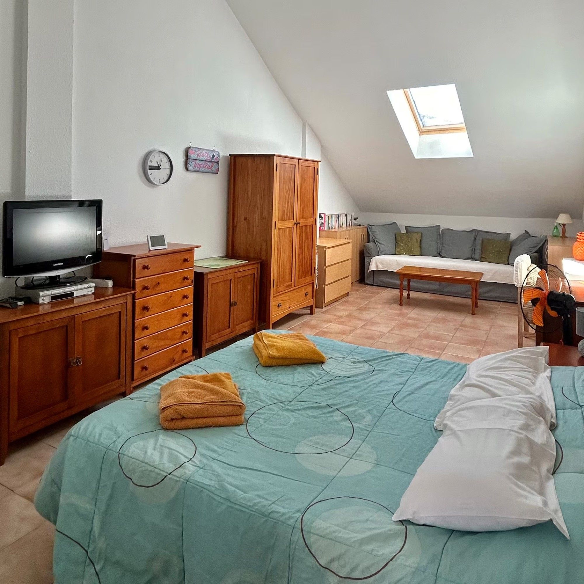 Une chambre à coucher comprenant un lit, une télévision, des meubles en bois, une lucarne et un canapé.