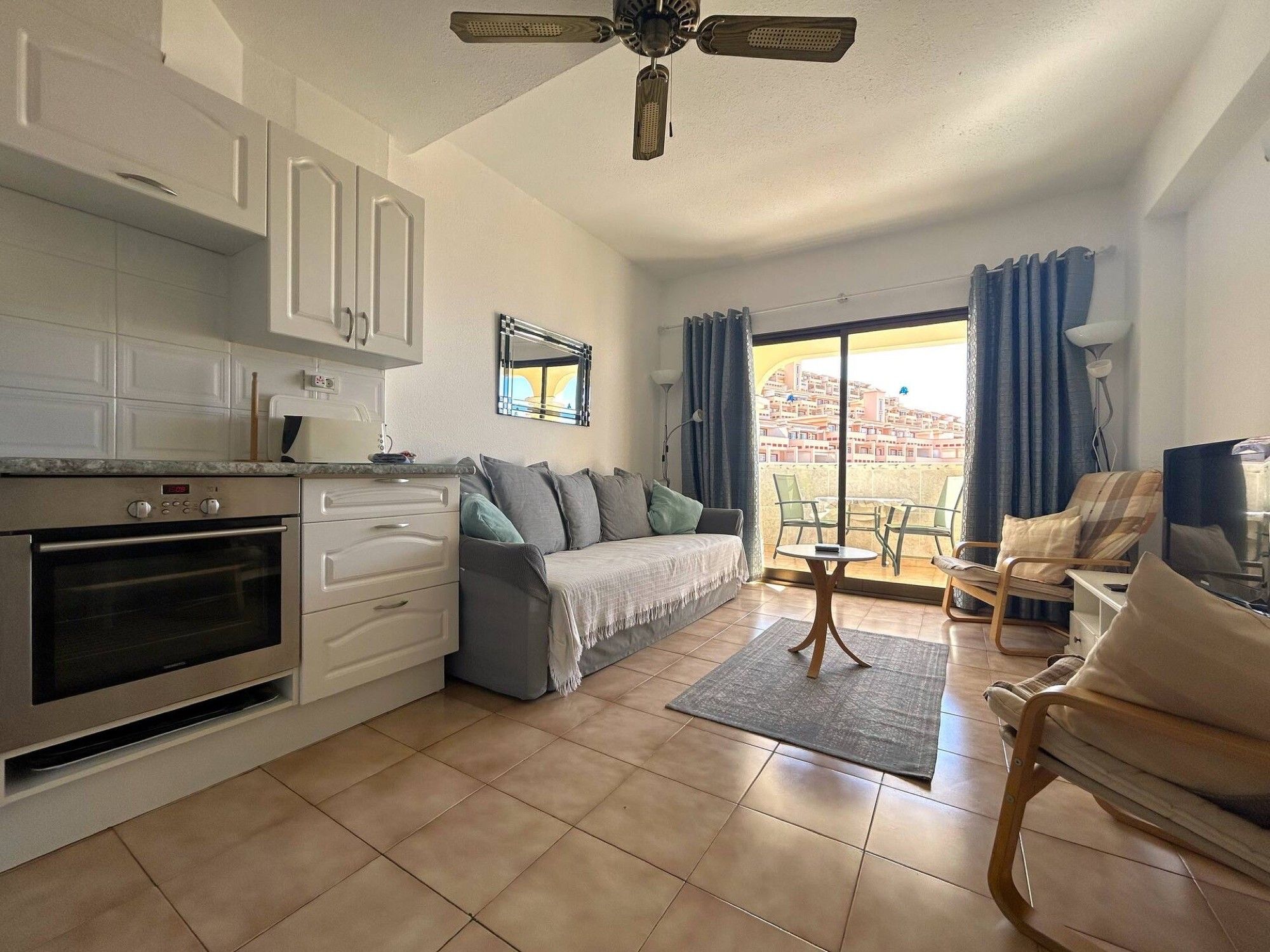 A compact living space with a kitchenette, a sofa, a dining area, and a balcony with a city view.