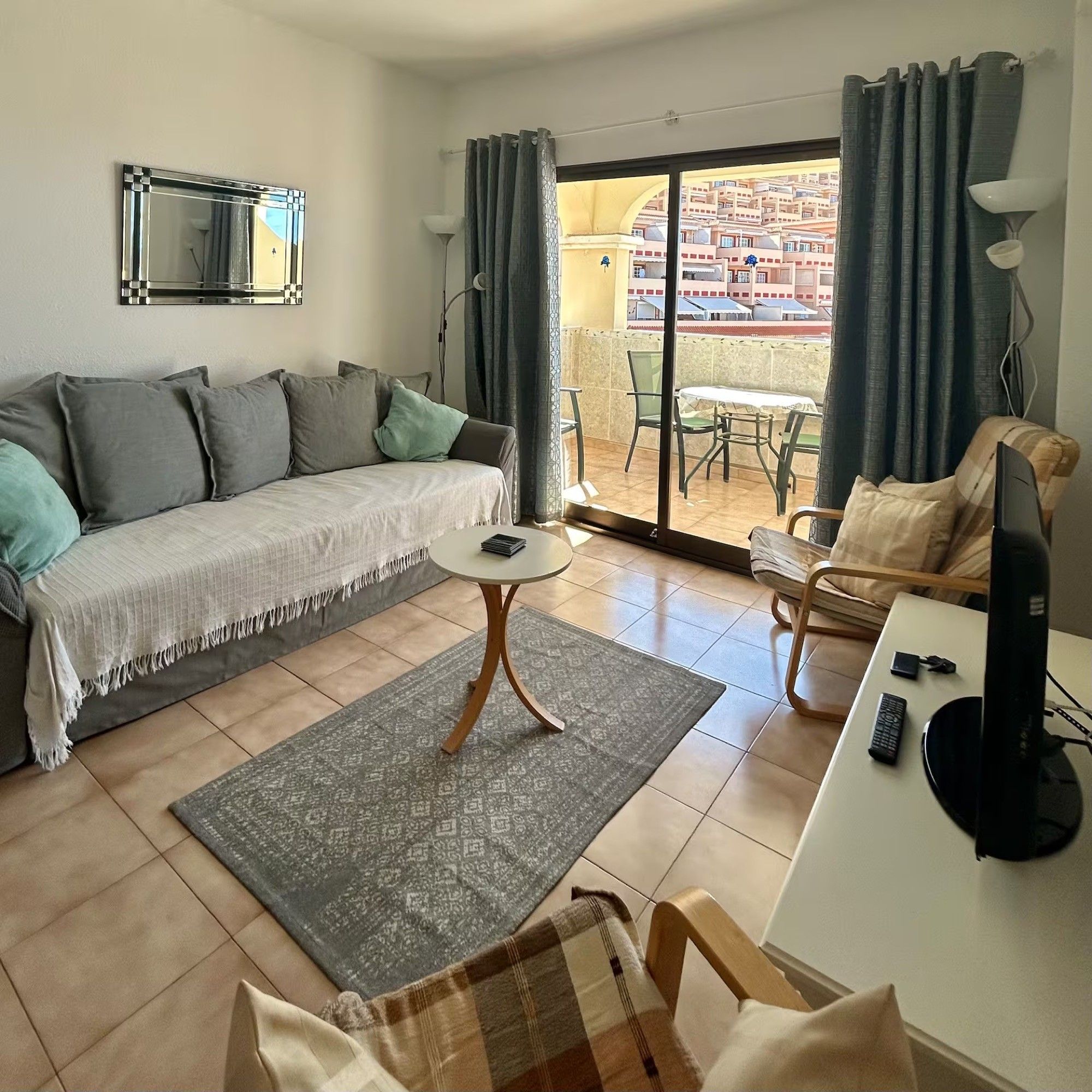 Un salon comprenant un canapé, une table basse, un téléviseur et un balcon avec vue sur les immeubles.