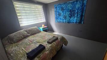 A bedroom with a bed, a nightstand, a window with blinds, and a blue tapestry on the wall.