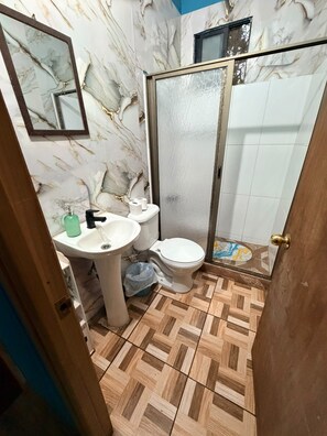 A bathroom with a marble wall, a sink, a toilet, and a shower area. - CABAÑA FAMILIAR 3 HABITACIONES (Hanga Roa)