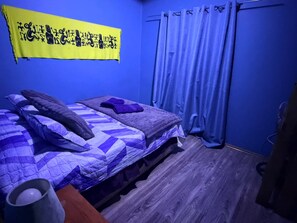 A room with a bed, a curtain, and a wall hanging. - CABAÑA FAMILIAR 3 HABITACIONES (Hanga Roa)