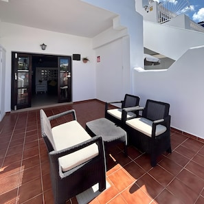 Un patio exterior con mobiliario de mimbre y suelo de baldosas.