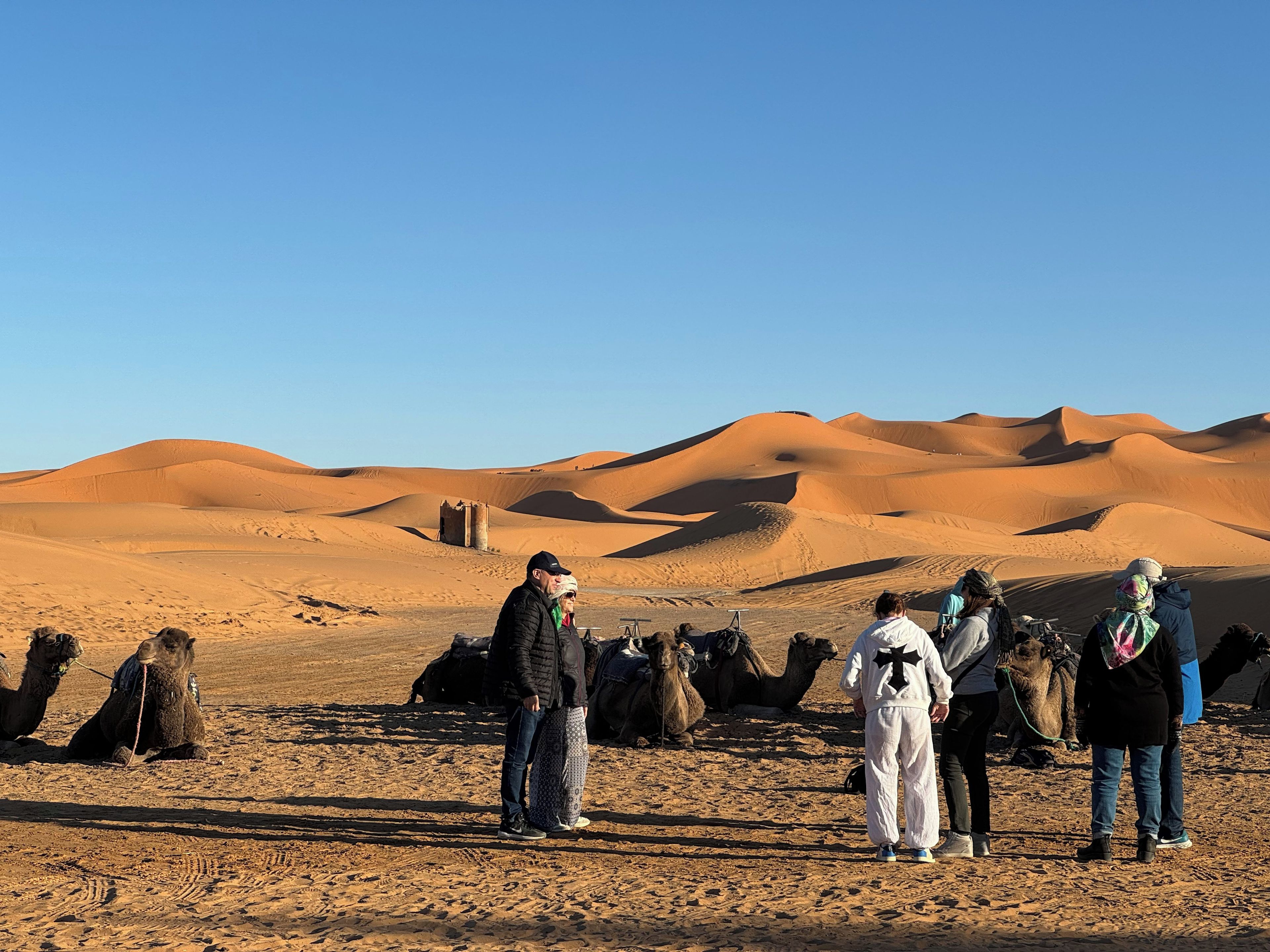 Grupo de pessoas em paisagem desértica com dunas de areia e camelos.