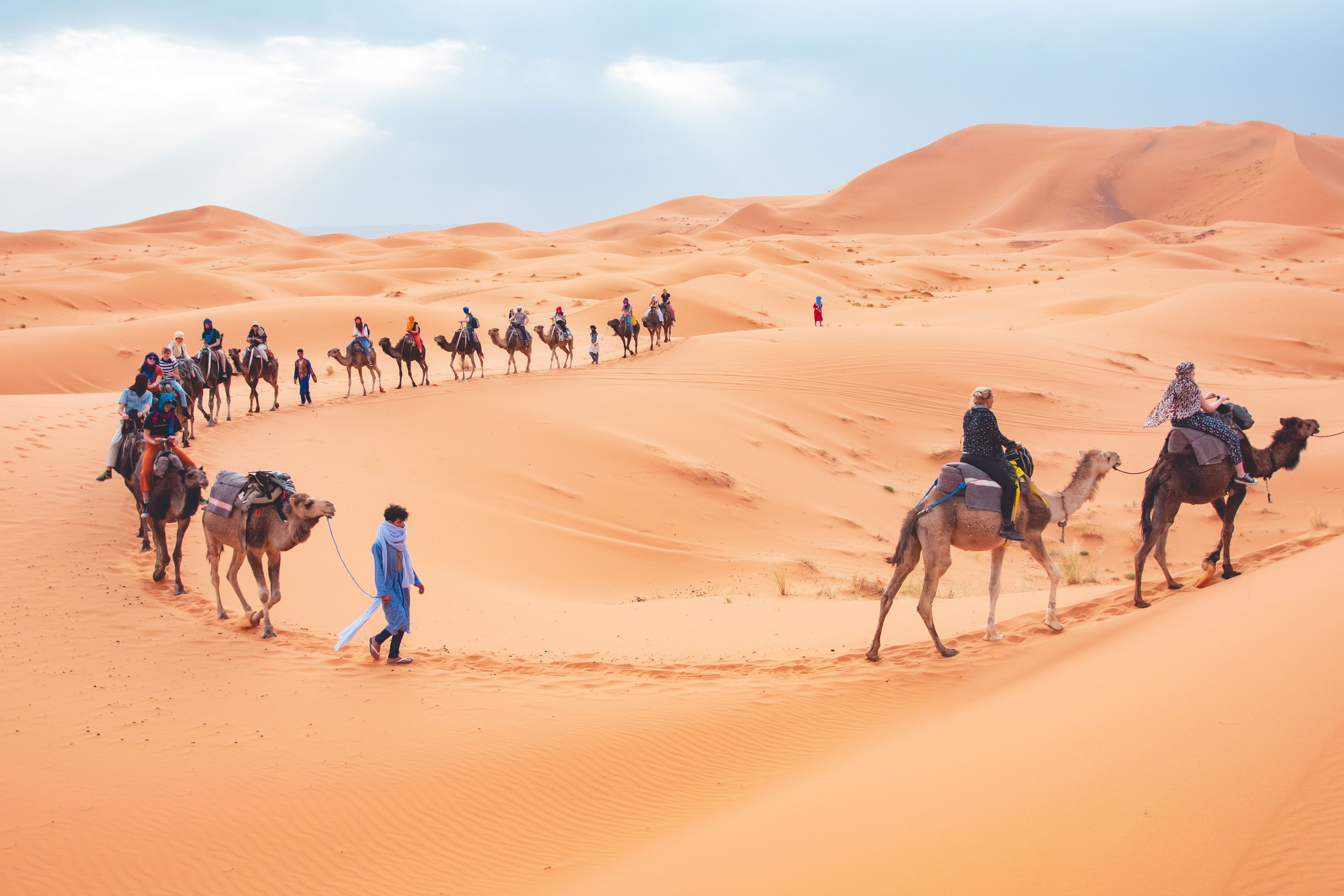 Un grupo de personas montando camellos a través de un paisaje desértico con dunas de arena.