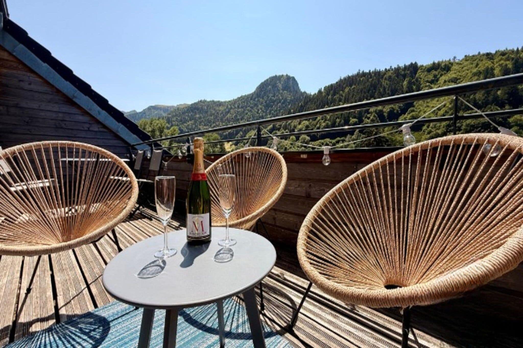 A wooden deck with wicker chairs, a table, and a bottle of wine.