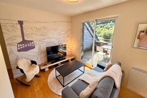 A modern living room with a sofa, a coffee table, a TV, and a fireplace. - Lush Apartment with Sancy Views (Mont-Dore)