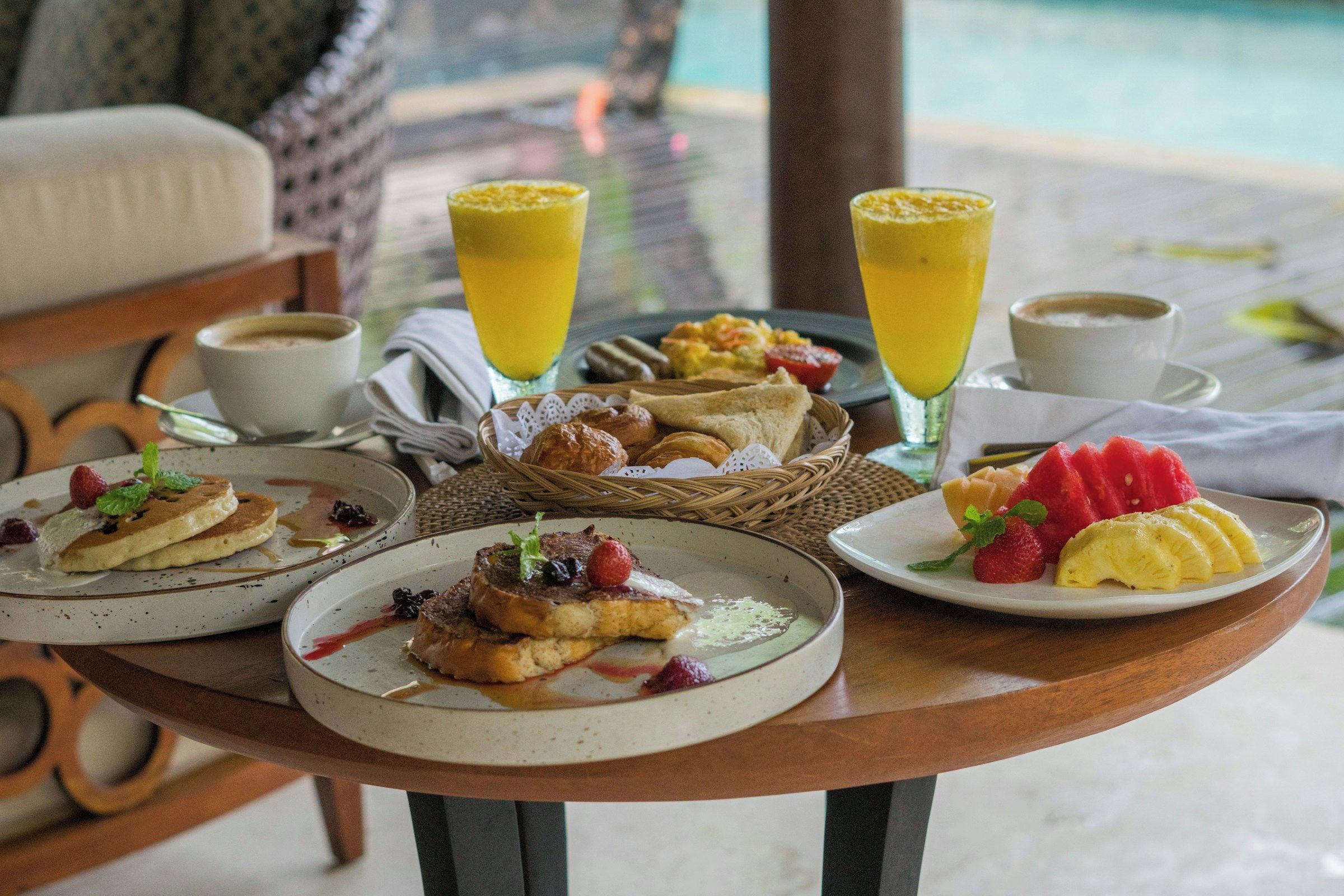 A breakfast setting with various dishes, drinks, and a view of a pool.