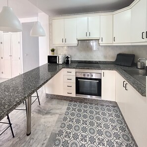 A modern kitchen with white cabinets, a granite countertop, a built-in oven, and a patterned backsplash. - 2 Bedroom apartment in Los Cristianos K210 (Oasis del Sur)