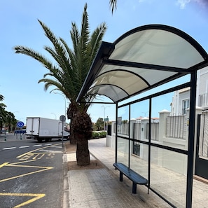 Una parada de autobús con refugio, una palmera y un camión blanco en la carretera.