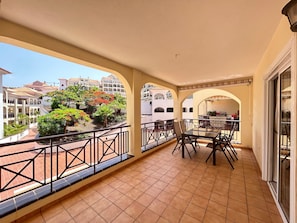 Un balcón con suelo de baldosas, una mesa con sillas y vistas a edificios y vegetación.
