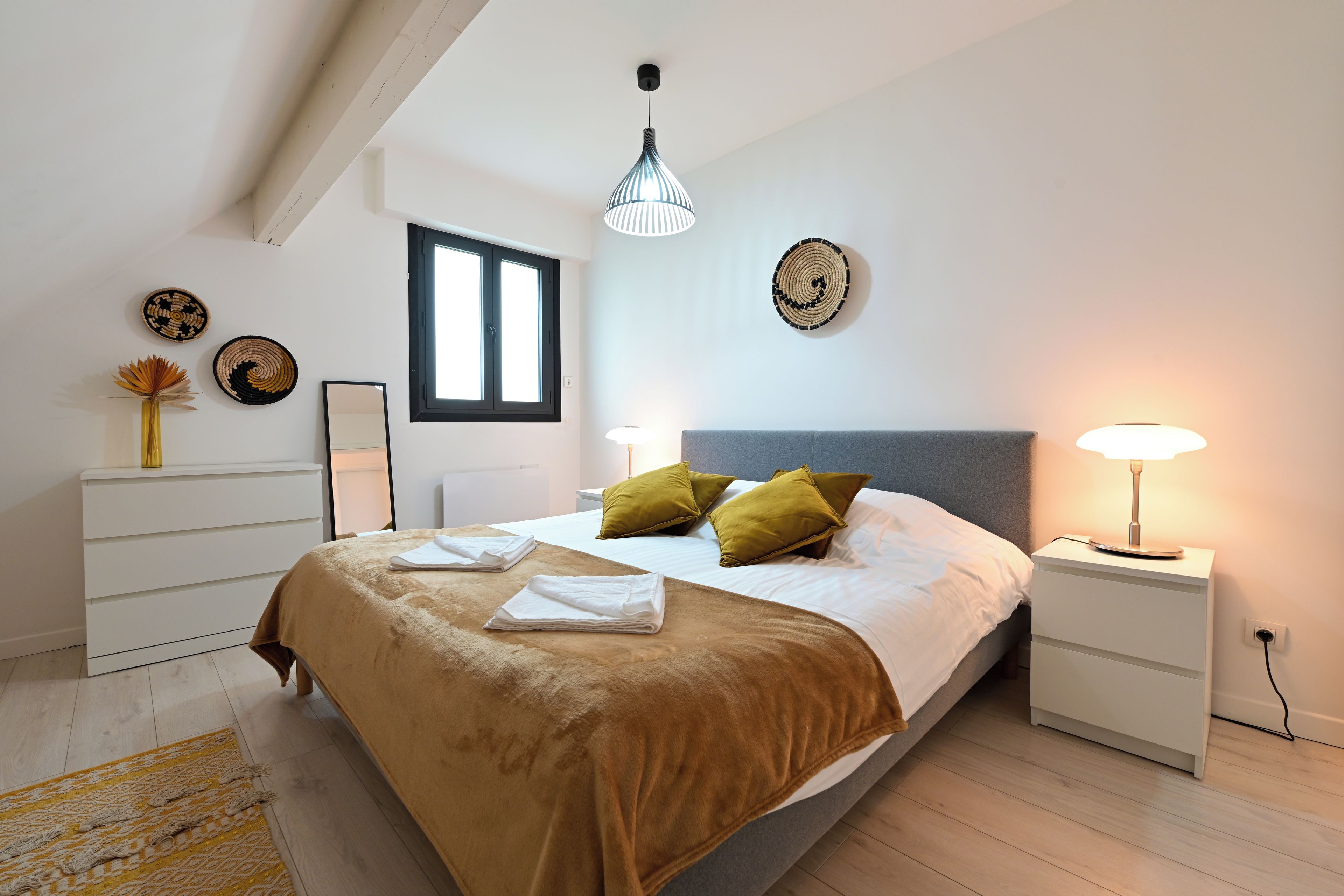 Un dormitorio moderno con cama, lámparas de noche, ventana y un adorno en la pared.