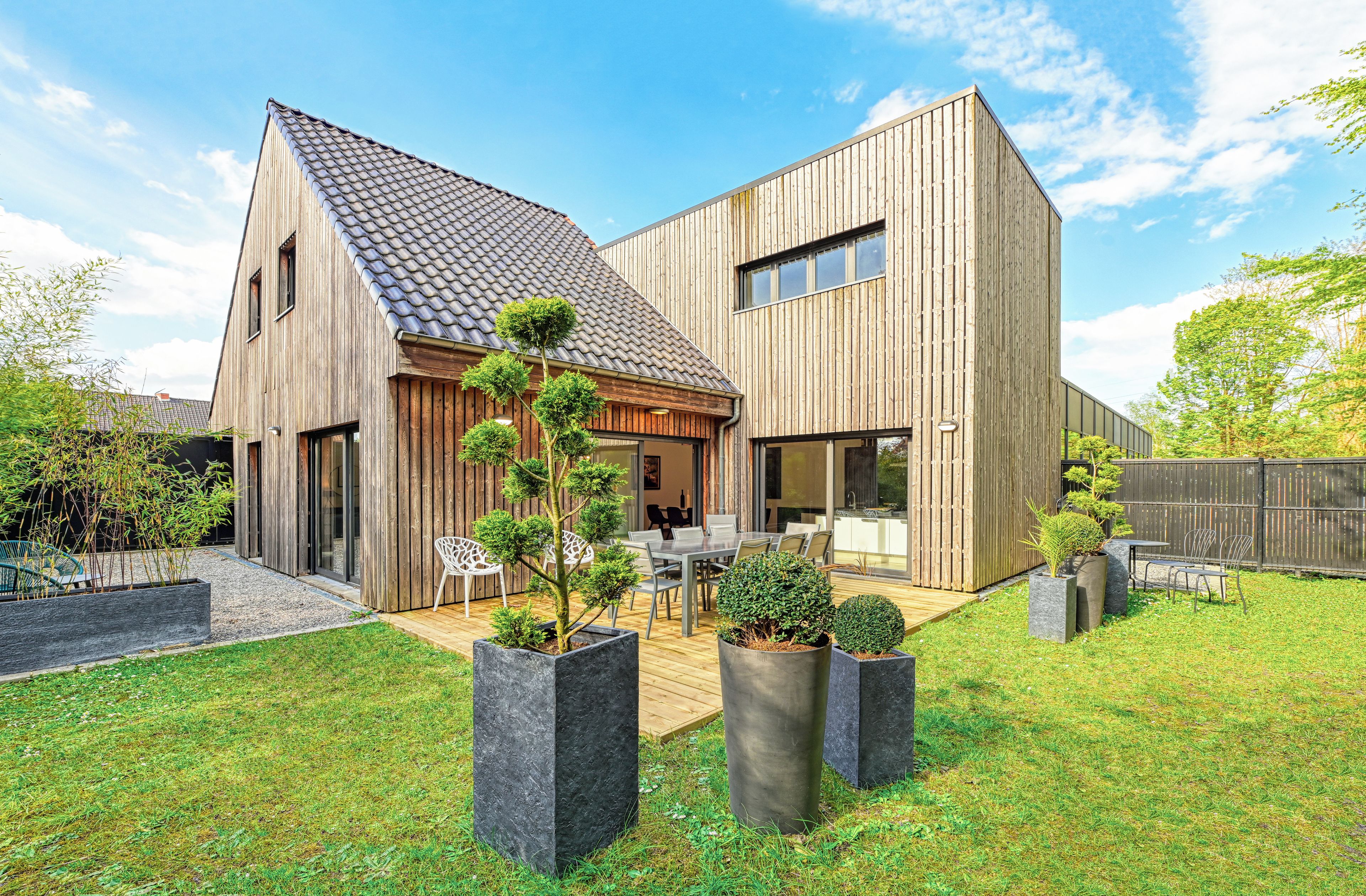 A modern two-story house with a sloped roof, a deck, and a well-maintained lawn.