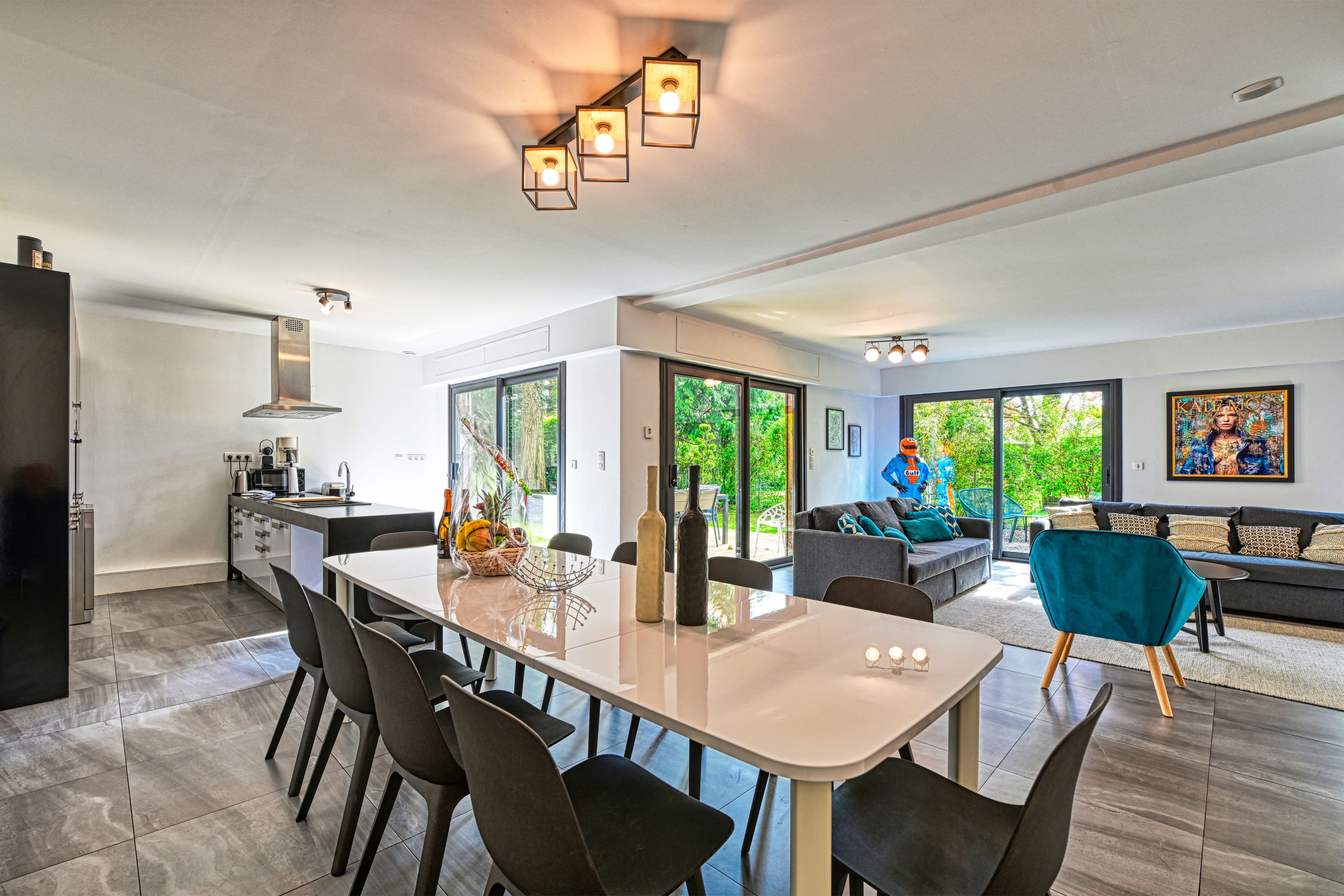 Eine moderne Küche mit Essbereich, großen Fenstern und einem Wohnzimmer mit Sofa und Kunstwerken.