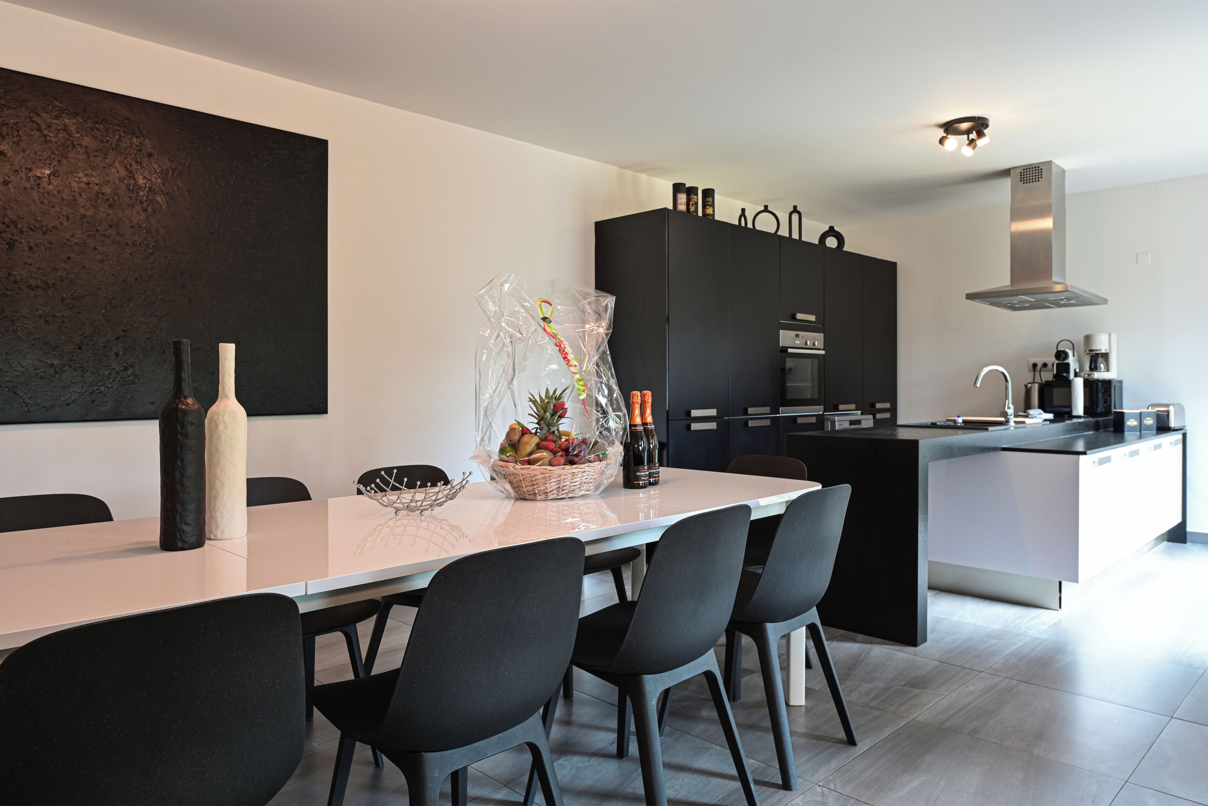 Eine moderne Küche mit Essbereich, ausgestattet mit einem weißen Tisch, schwarzen Stühlen und einem großen schwarzen Schrank.