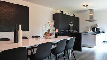 Eine moderne Küche mit Essbereich, ausgestattet mit einem weißen Tisch, schwarzen Stühlen und einem großen schwarzen Schrank.