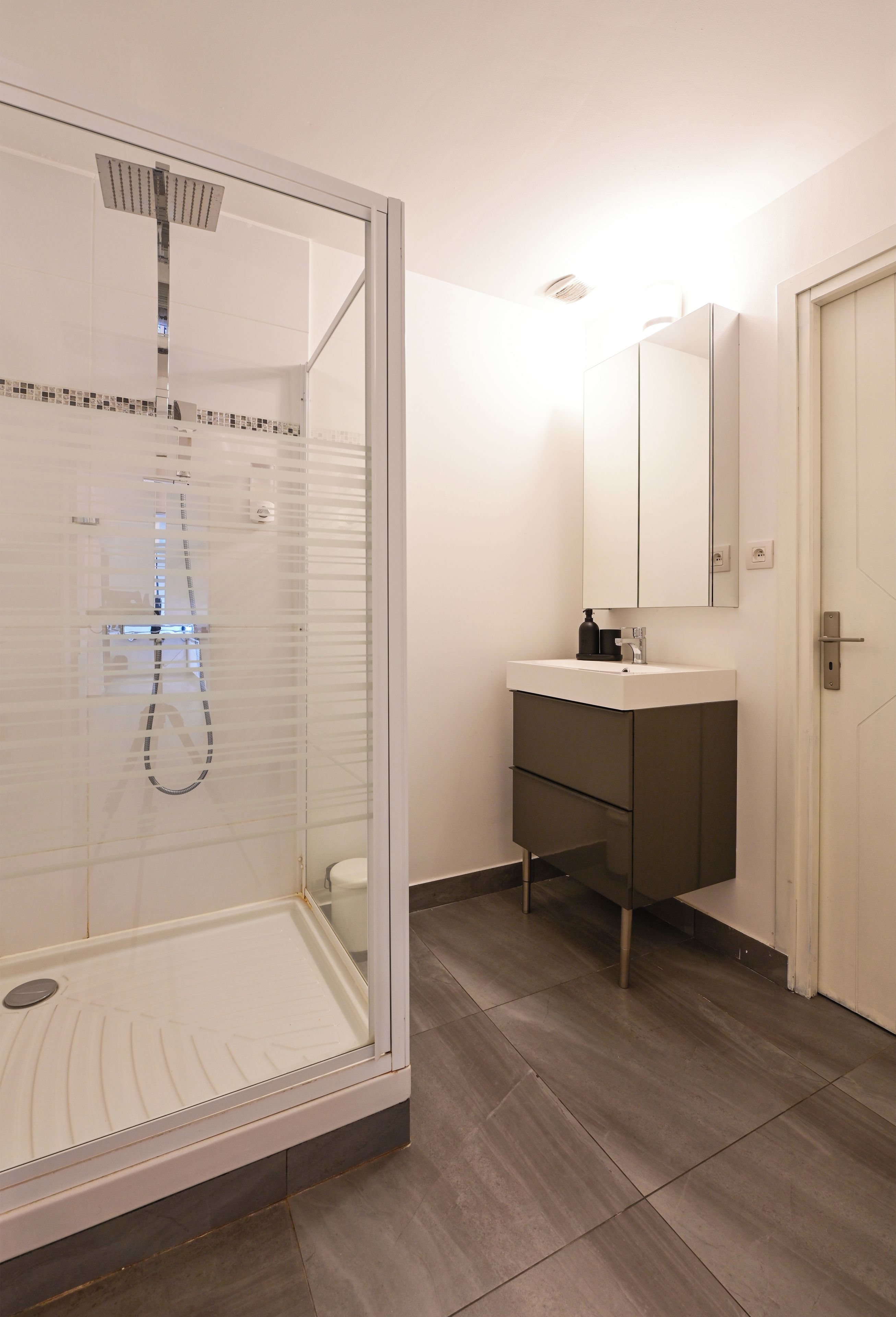 Une salle de bain moderne avec une douche à parois de verre, un lavabo blanc et un miroir au-dessus.