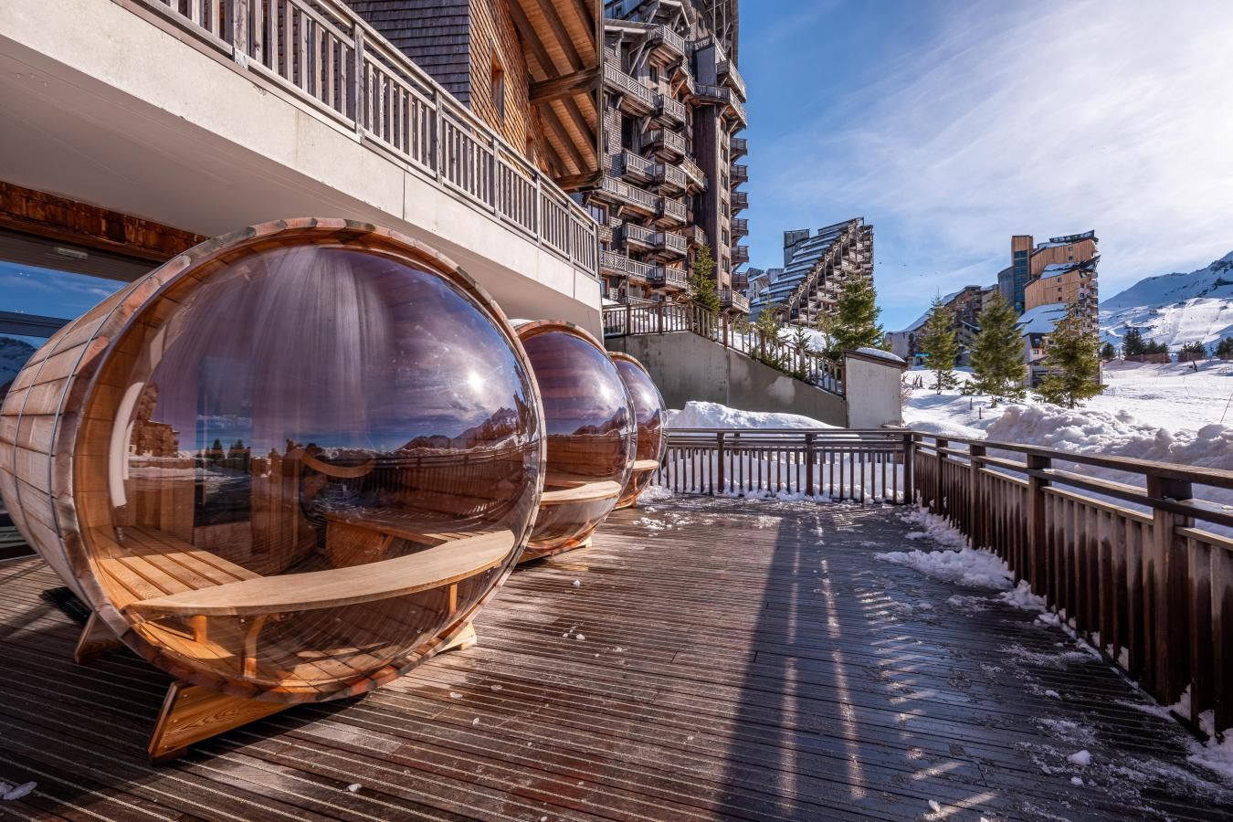 A wooden deck with transparent cylindrical structures, a wooden fence, and a snowy landscape with buildings in the background.