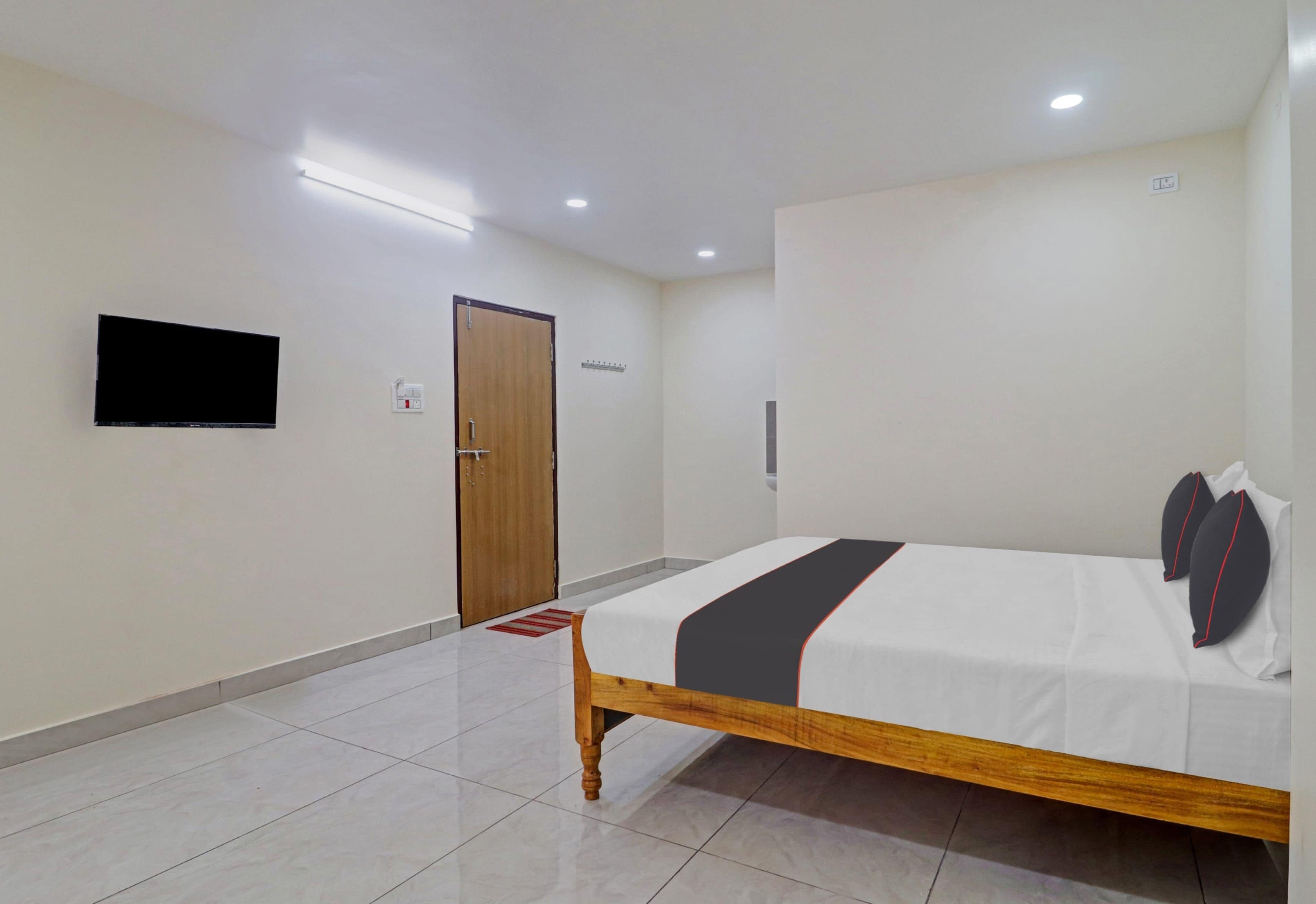 Quarto de hotel com cama, televisão, porta e chão de azulejos.