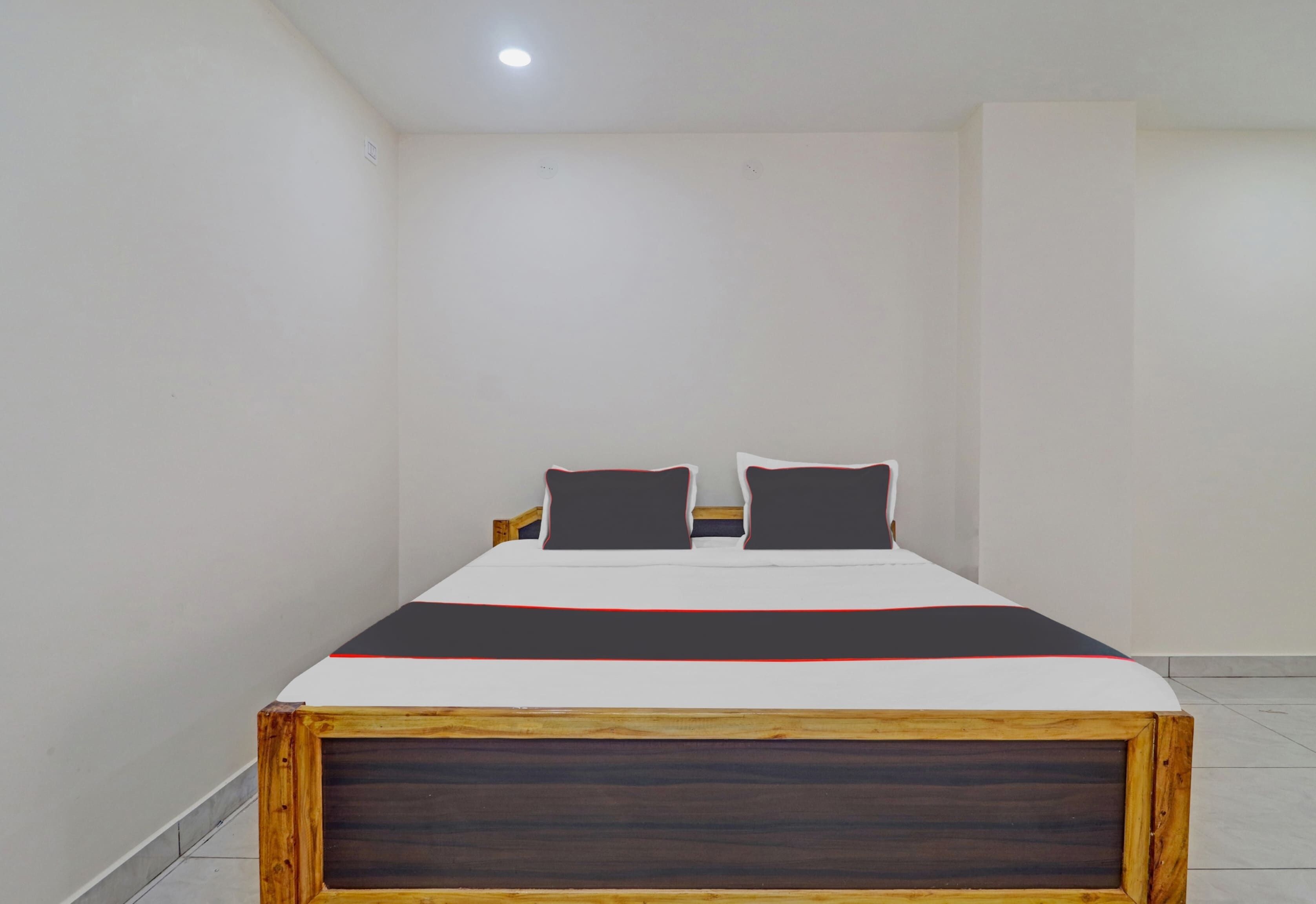 Quarto individual com uma cama de solteiro, cabeceira de madeira, paredes brancas e iluminação no teto.