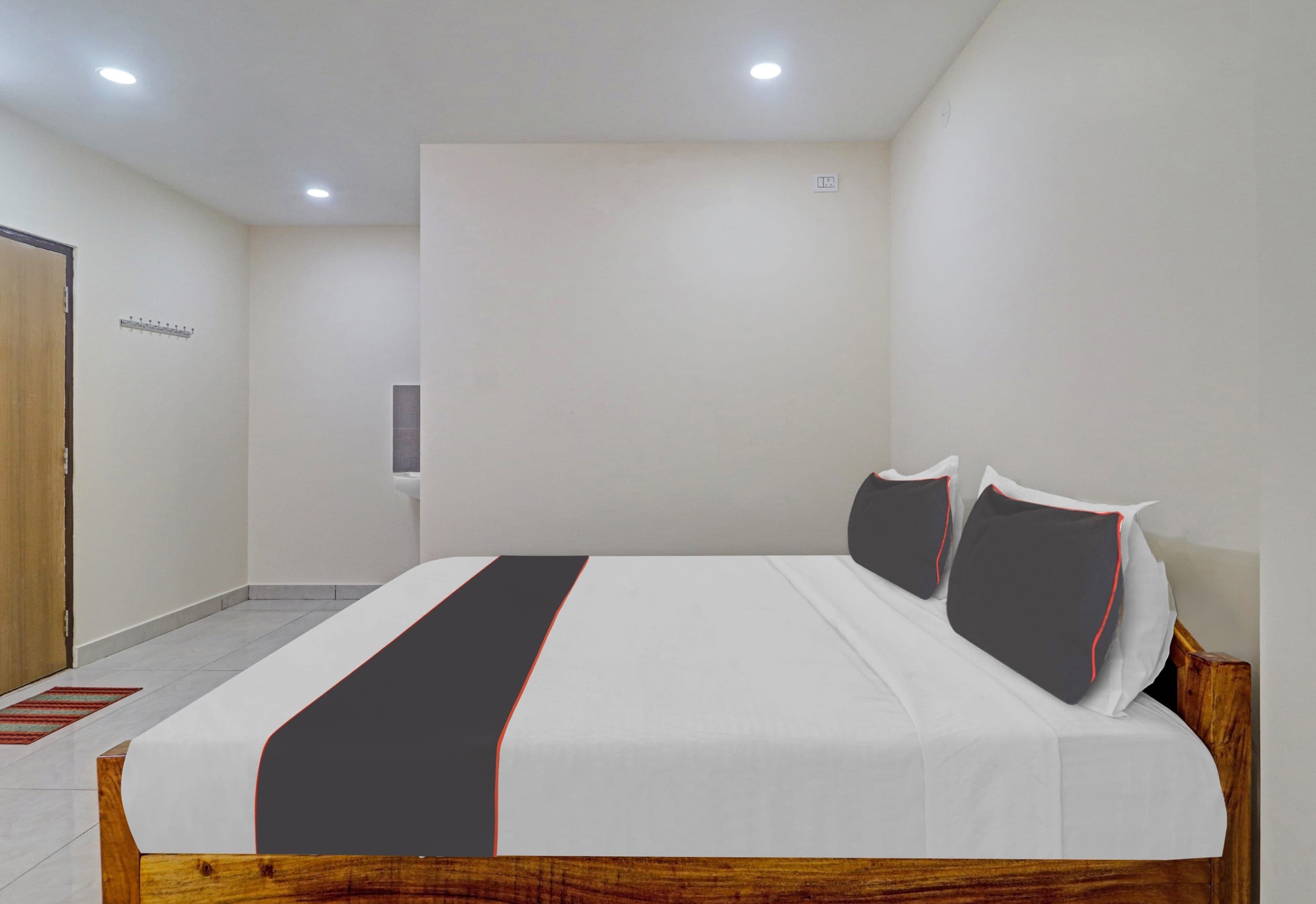 A modern hotel room with a large bed, a wooden headboard, a small bedside table, and a wall-mounted light fixture.