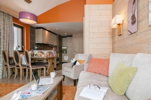 A modern living room with a sofa, a dining table with chairs, a kitchen area, and a wooden wall with a poster. - Wifi, 10m from ski slopes, fitness, swimming pool, sauna, hammam, balcony, ski locker, 63-68m² (Avoriaz)