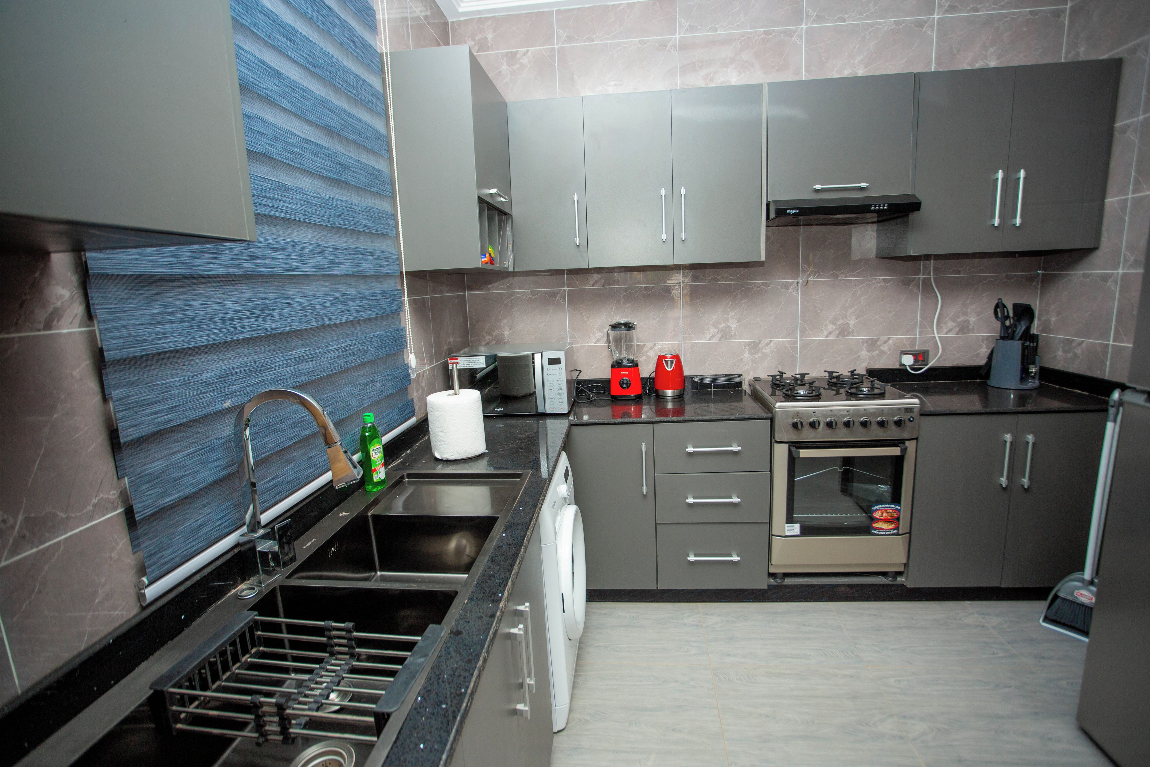A modern kitchen with grey cabinets, a stainless steel sink, a dishwasher, a stove, and a microwave.