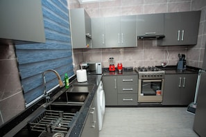 A modern kitchen with grey cabinets, a stainless steel sink, a dishwasher, a stove, and a microwave.