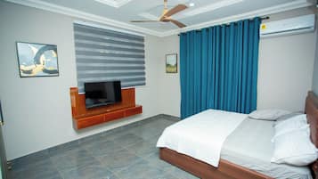 A bedroom with a bed, a television mounted on the wall, a ceiling fan, and a window with curtains.