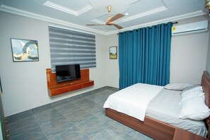 A bedroom with a bed, a television mounted on the wall, a ceiling fan, and a window with curtains.