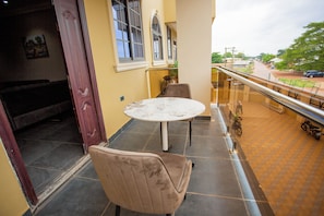 A balcony with a round table and two chairs, overlooking a street with parked cars and greenery. - Gateway Lodge Tamale Ghana (Tamale)