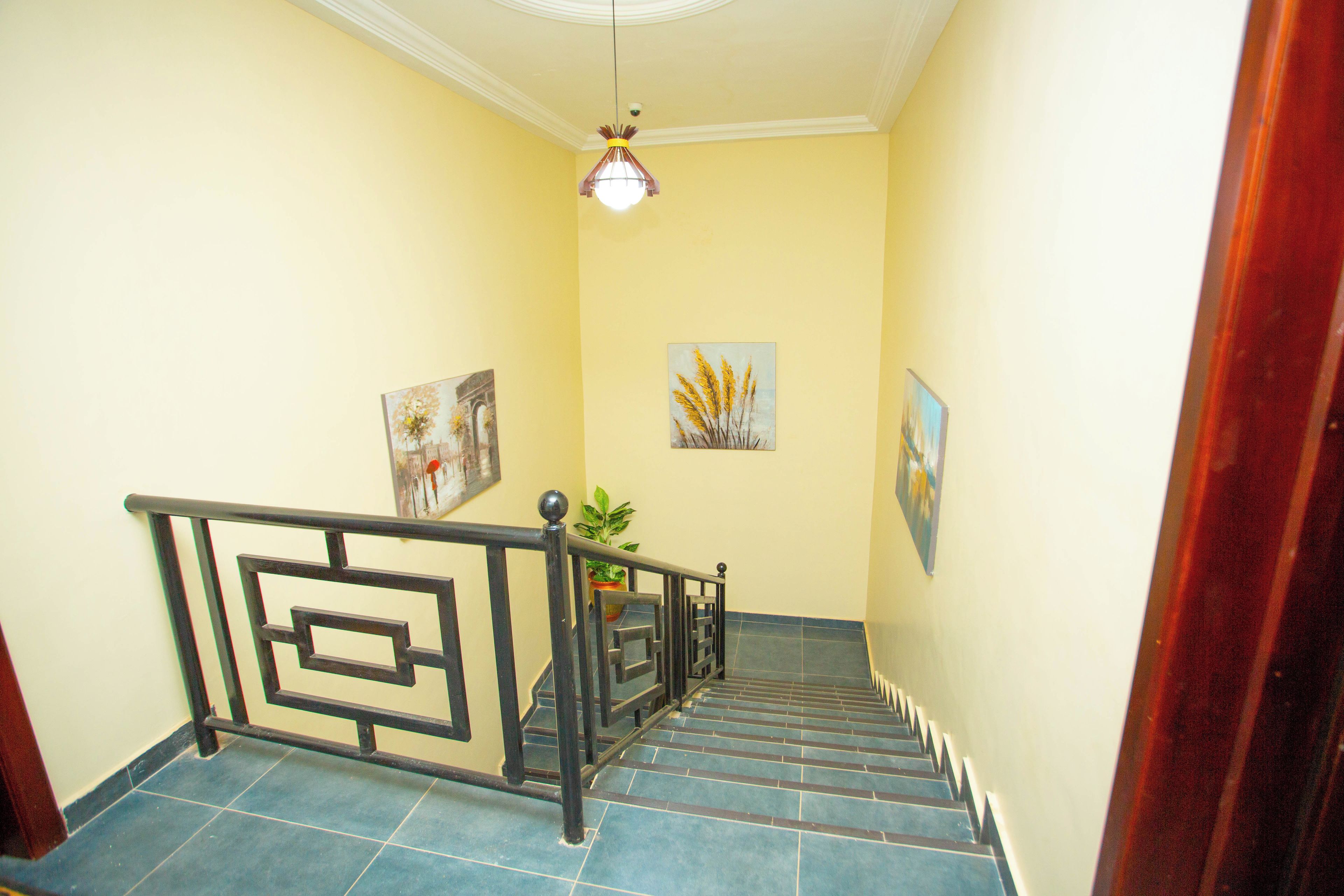 Eine Treppe mit einem geometrischen Geländer, einem Blumentopf und zwei an der Wand befestigten Gemälden.