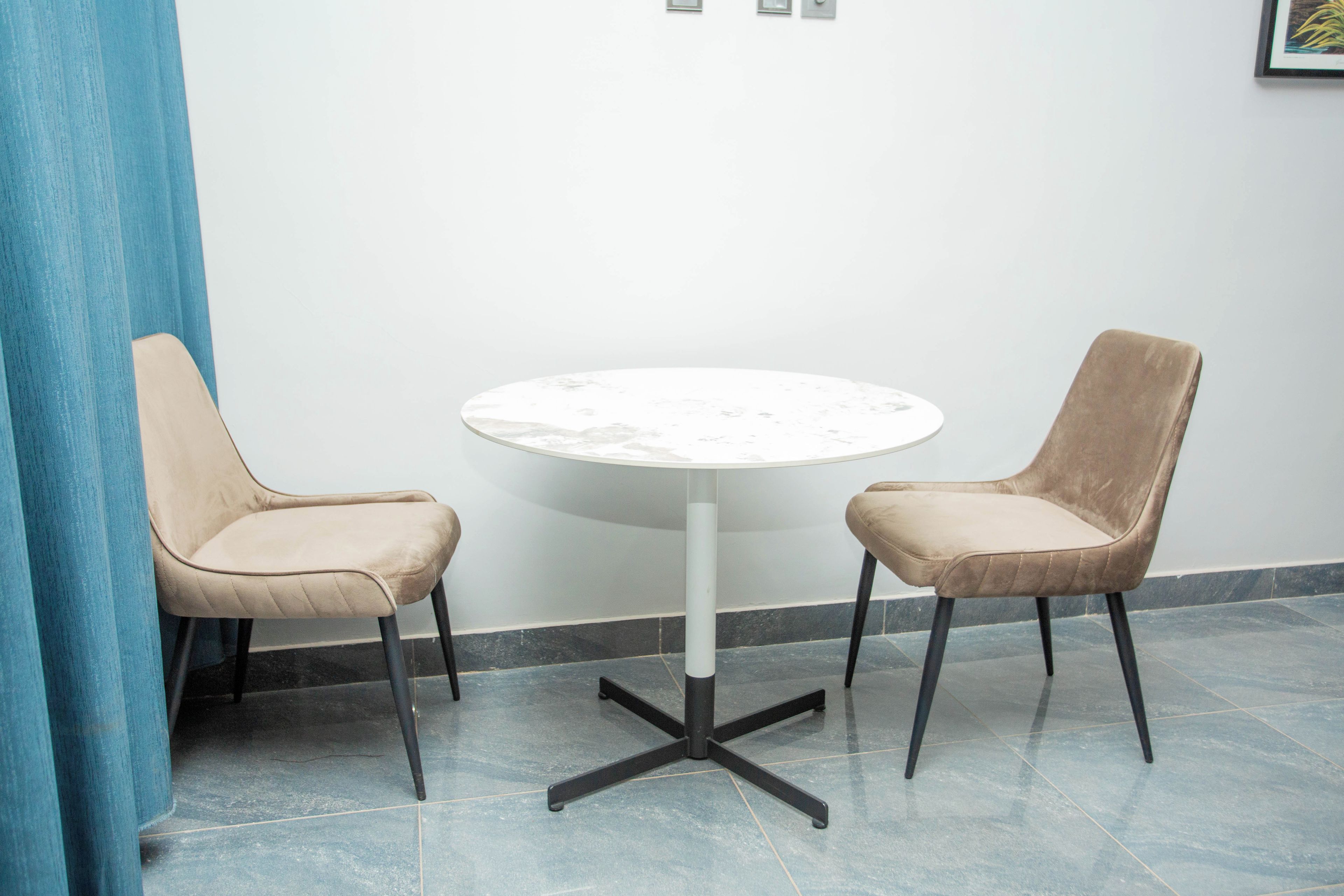 A round table with a marble top and black metal legs, flanked by two beige upholstered chairs with black metal legs.