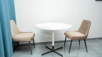 A round table with a marble top and black metal legs, flanked by two beige upholstered chairs with black metal legs.