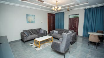 A living room with a sofa set, a coffee table, a dining table with chairs, a chandelier, and a ceiling fan.