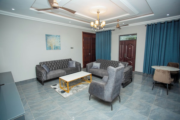 A living room with a sofa set, a coffee table, a dining table with chairs, a chandelier, and a ceiling fan.