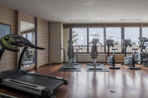Un gimnasio con equipo de cardio, cinta de correr y vistas a montañas a través de amplias ventanas.