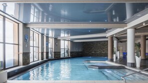 Una piscina interior con paredes de vidrio transparente, muros de piedra y un diseño moderno.