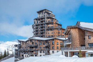 Un hotel de varios pisos con un diseño arquitectónico singular, con balcones y una pista de esquí al fondo.