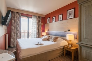 A hotel room with a bed, a bedside table with a lamp, a TV mounted on the wall, and a window with curtains. - Wifi, 10m from ski slopes, fitness, swimming pool, sauna, hammam, balcony, ski locker, 87-98m² (Avoriaz)