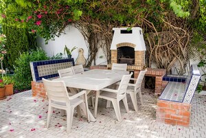 Un patio al aire libre con horno de ladrillo, mesa y sillas blancas.