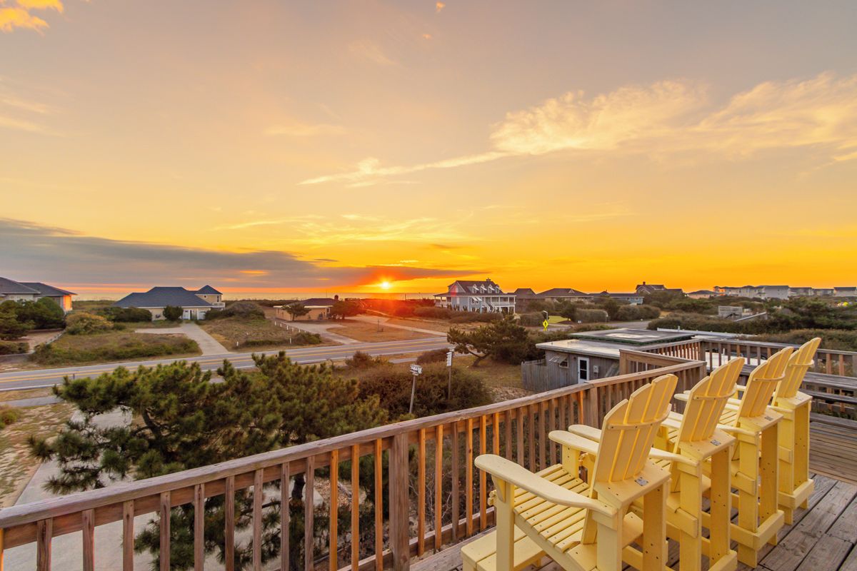 Une vue sur le coucher de soleil depuis un balcon doté de balustrades en bois et de chaises Adirondack jaunes.