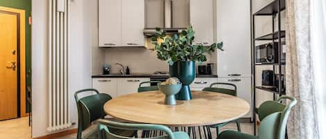 Una cocina moderna con armarios blancos, una mesa redonda de madera y sillas verdes.