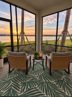 A balcony with wicker chairs, a small table, and a view of a sunset over a body of water. -  Gorgeous views !!! 3-bedroom condo in a golf community in lakewood Ranch. (Bradenton)