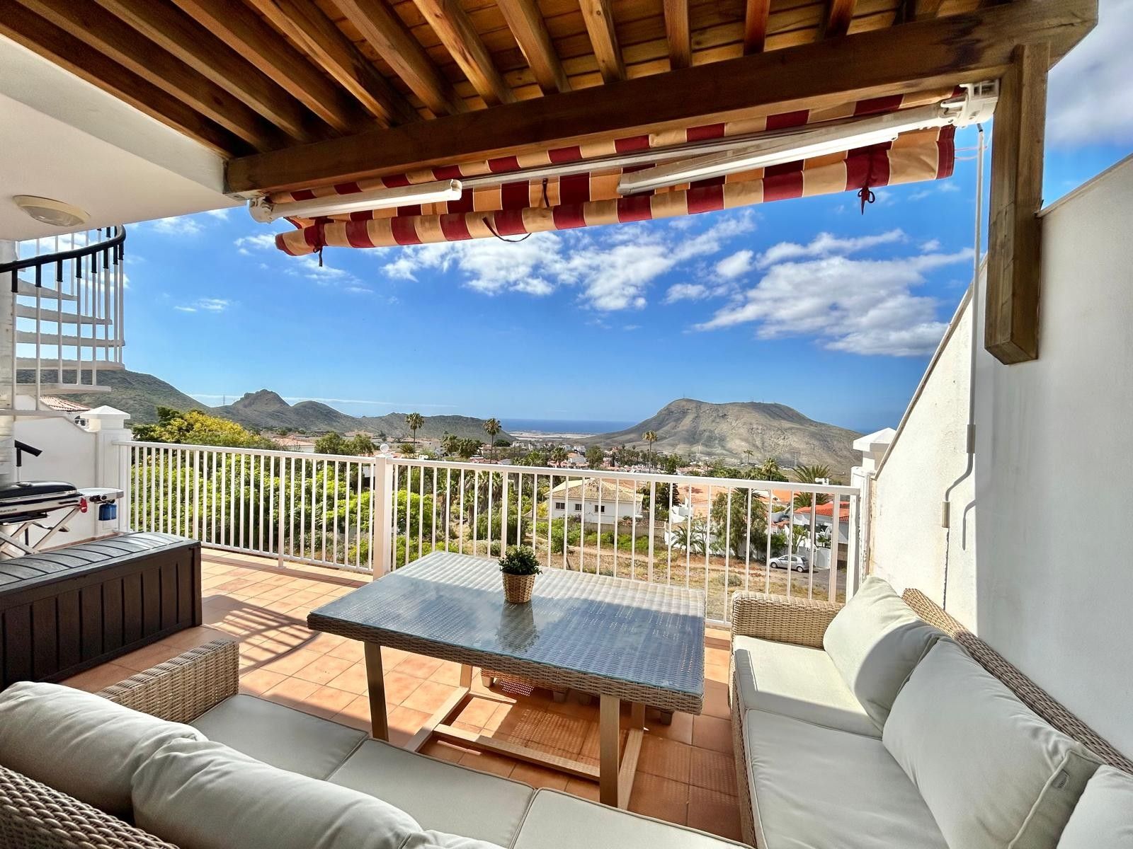 A balcony with a table and chairs, a view of the landscape, and a wooden ceiling.