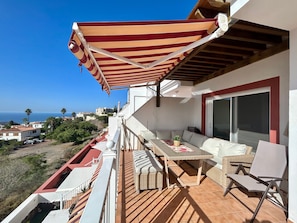 Een balkon met een gestreepte zonnescherm, buitenmeubilair en uitzicht op zee.