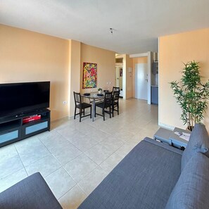 Een moderne woonkamer met een flatscreen televisie, een eethoek met een tafel en stoelen, een bank en een potplant.