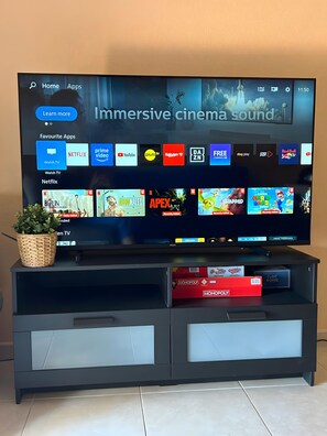 A television on a black entertainment unit with a woven basket and Monopoly game boxes. - Vacation Home 'Sea View 1 Bedroom Chayofa K109' with Mountain View, Shared Pool and Wi-Fi (Arona)